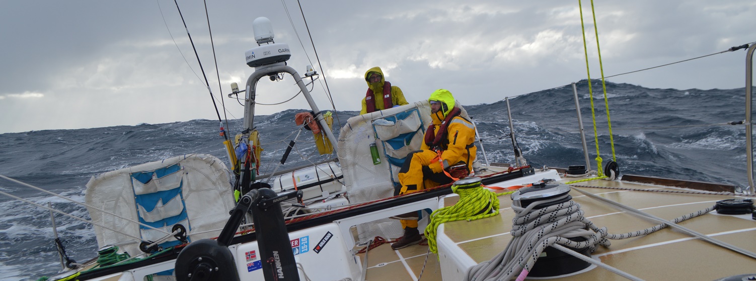 Crew shown helming on board Garmin heeled over with big following seas 