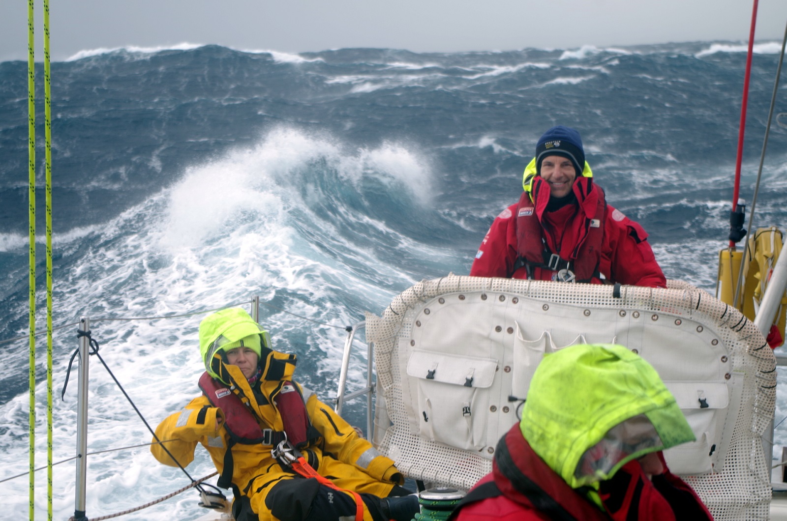 Crew member shown smiling on the helm with large waves behind him 
