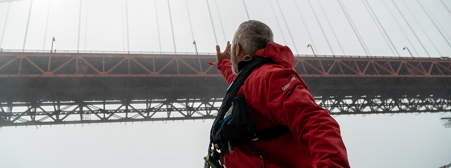 Qingdao Crew, Jody Shaw, looks up at the Golden Gate Bridge as the yacht completes Race 10
